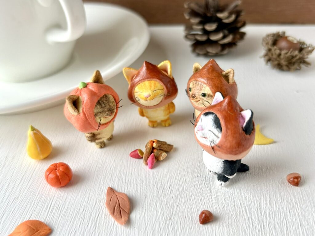 栗を被った猫さんとカボチャをかぶった猫さんが4人で焚火をして焼き芋を作っている飾り方事例。手のひらサイズの粘土製の置物。