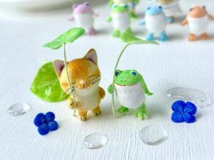 猫さんとカエルさんが仲良く葉っぱの傘をさして雨宿り