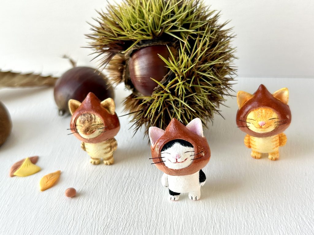 栗をかぶってにこにこしている小さな粘土製の猫トリオ